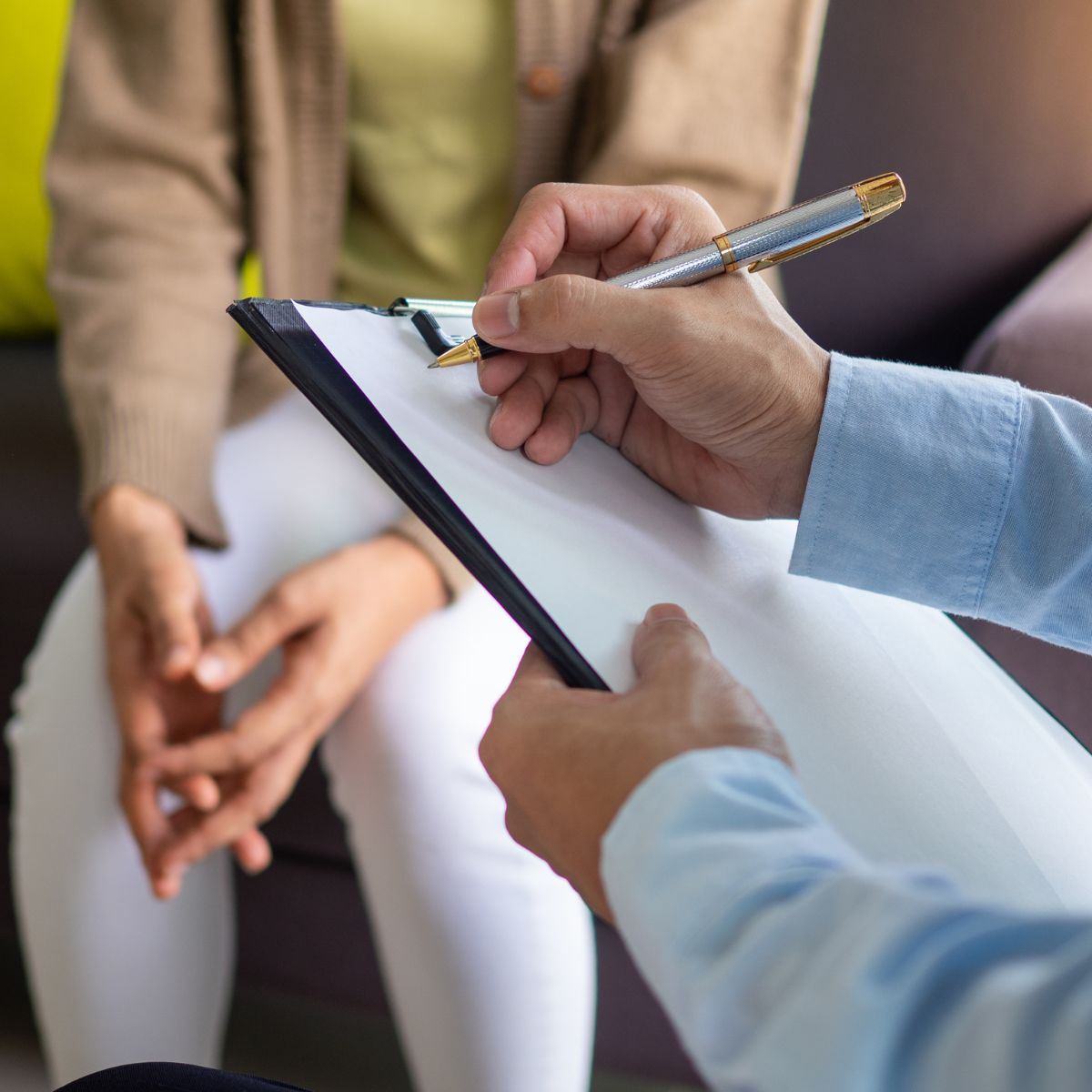 male therapist taking notes while speaking with a female patient.