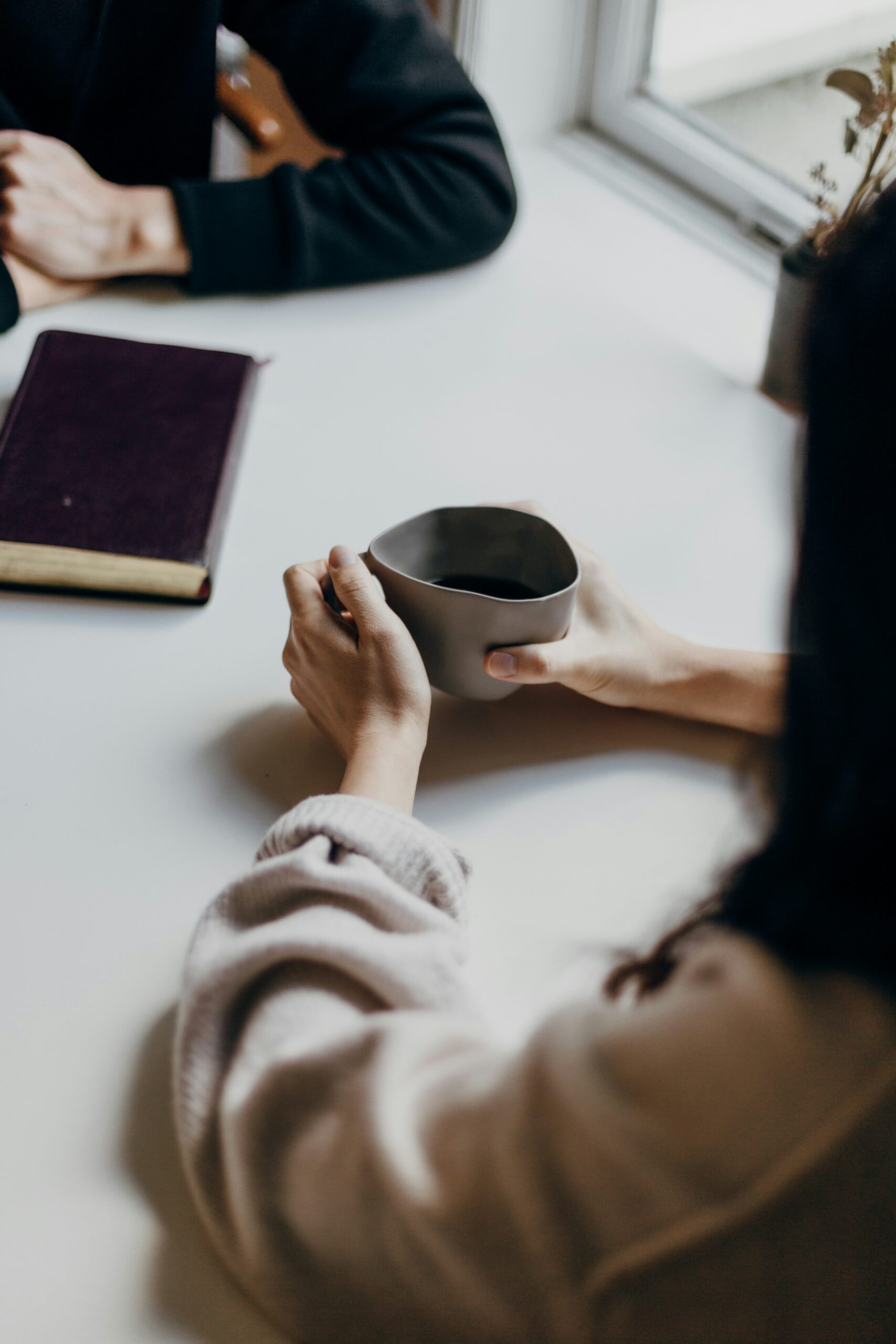 two people sitting across from each other. one holding a cup of coffee the other has a notebook in front of them